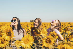 Three happy teenage girls with a with a reef safe sunscreen on their nose standing in a blossom sunflower farm.